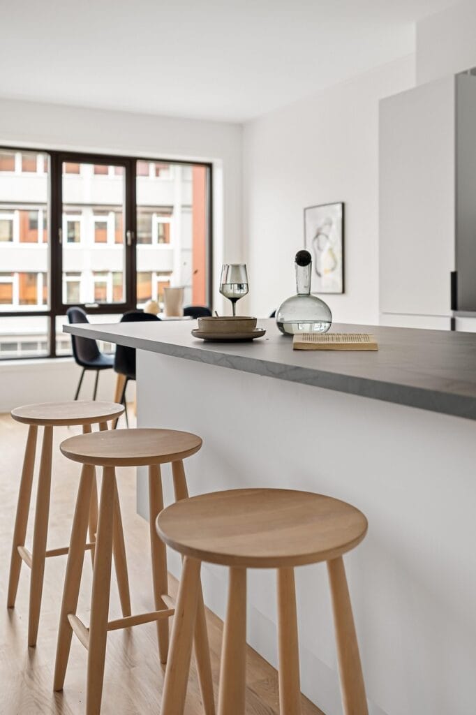 Cuisine contemporaine lumineuse – Agence Motte Cuisine ouverte moderne avec îlot central et tabourets en bois clair – bien immobilier