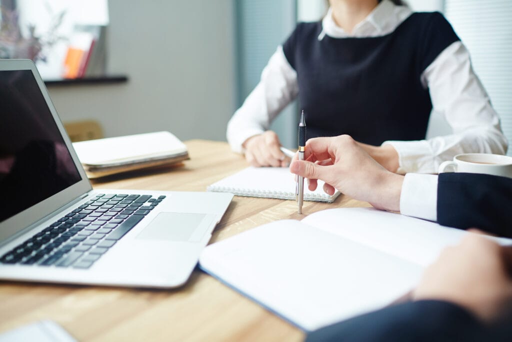 Rendez-vous en agence – Agence Motte Échange professionnel entre deux personnes avec ordinateur et carnet de notes