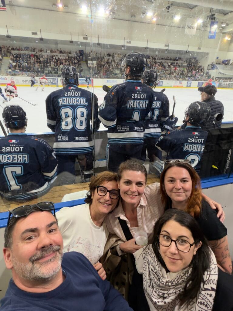 Équipe de l’agence réunie à la patinoire de Tours lors d’un match de hockey, avec les joueurs des Remparts visibles en arrière-plan.